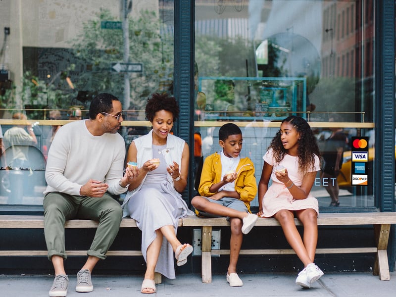 Mastercard logo sticker on shop window with a man, woman, and two childeren sitting on bench